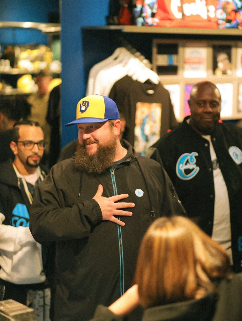 Person in a blue-and-yellow cap speaking inside a cannabis retail environment